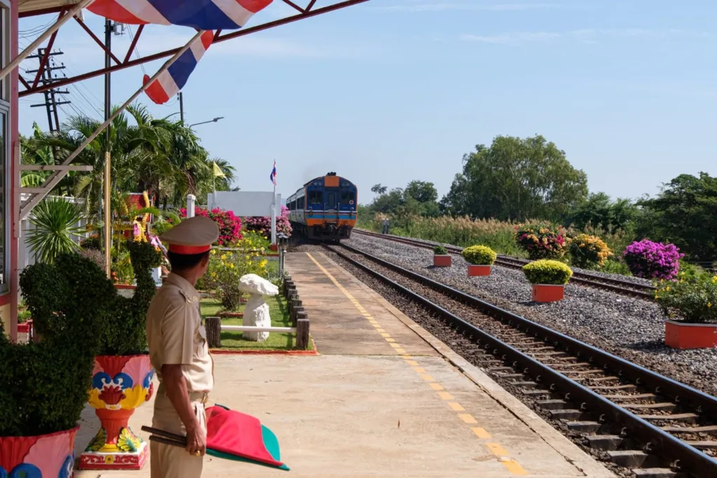 Thailand Public-Private Partnerships: Uniformed person stands by a colorful train station as a blue train approaches.