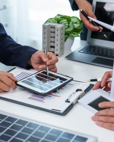 Team of business individuals engaged with a laptop and tablet, strategizing for a solar project.