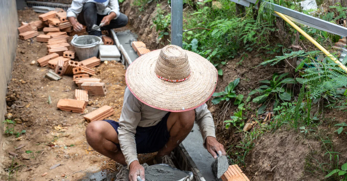 Two construction workers are laying down mason bricks, symbolising the shortage of Skilled Labor in Thailand Construction.