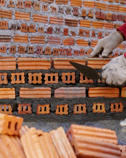 A worker constructs a wall using a brick, demonstrating skilled masonry techniques and Thailand Construction Costs.