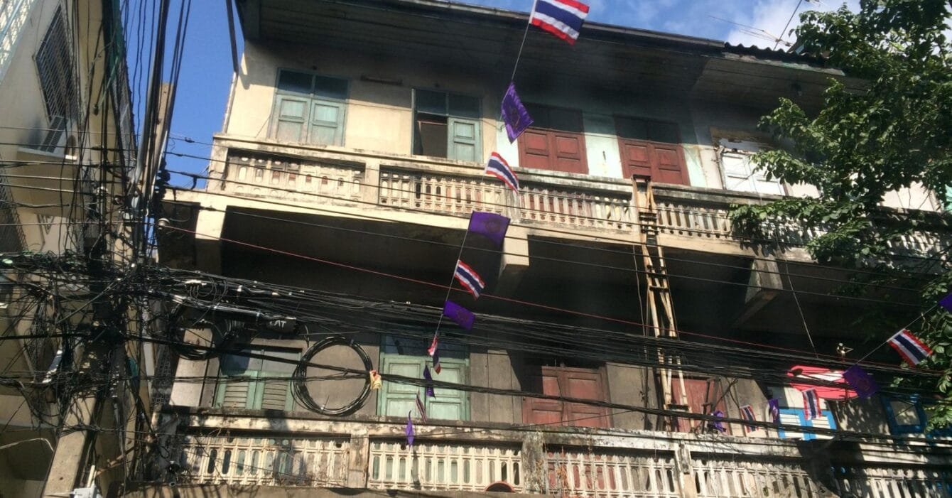 Thailand Affordable Housing Initiatives: Old building with tangled cables and hanging Thai flags.